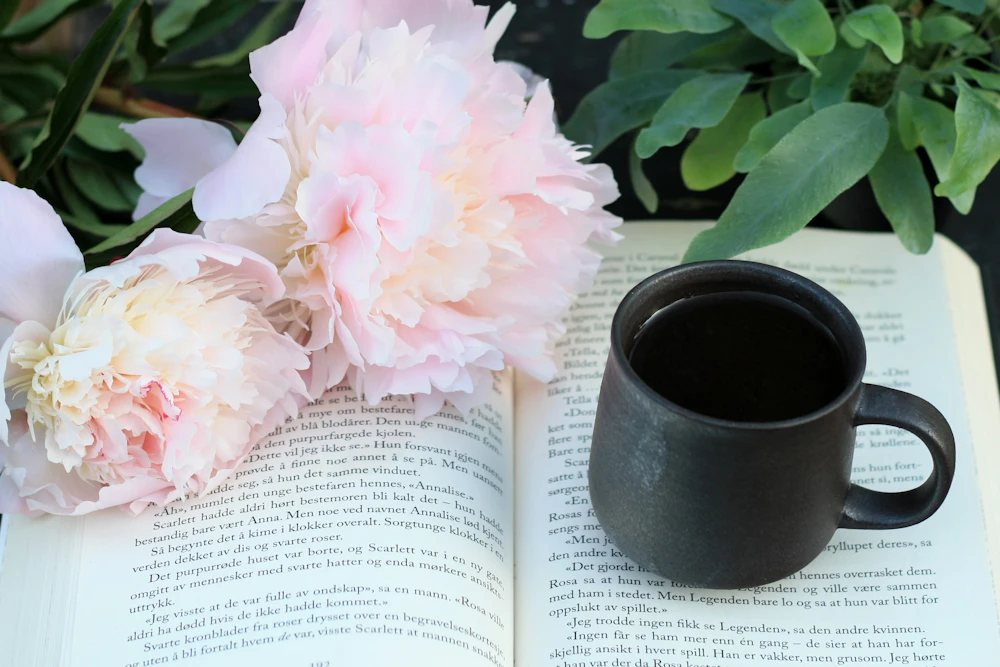 An open book, coffee and pink peonies on a table